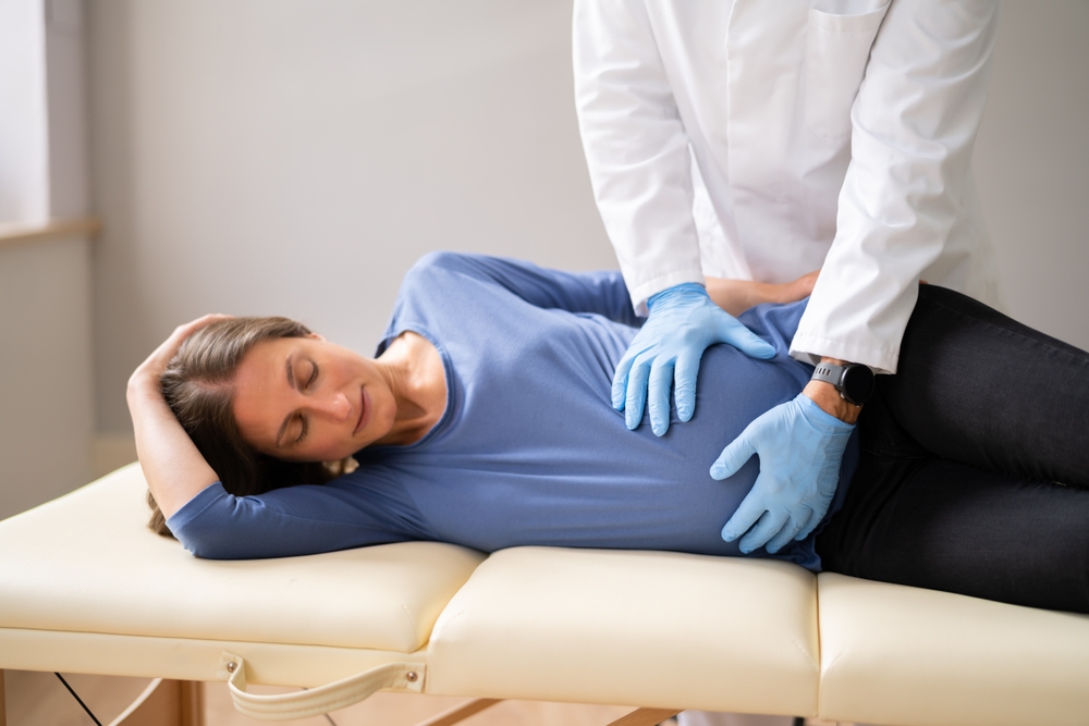 side view of a pregnant woman lying on an examination table with a clinician wearing gloves pressing her stomach.
