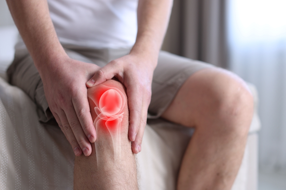 Close-up of a man holding his knee with both hands as a red glow highlights the patella and joint area indicating acute pain.