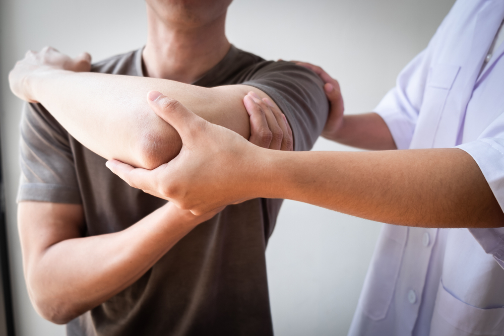 A healthcare provider in a white clinical coat performing a physical assessment on a patient's arm and shoulder to test for nerve compression and radiating symptoms related to spinal health.