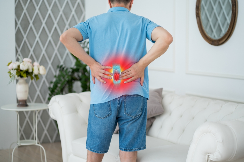 Rear view of a man holding his lower back with a red and blue glow highlighting the lumbar spine area signifying pain.