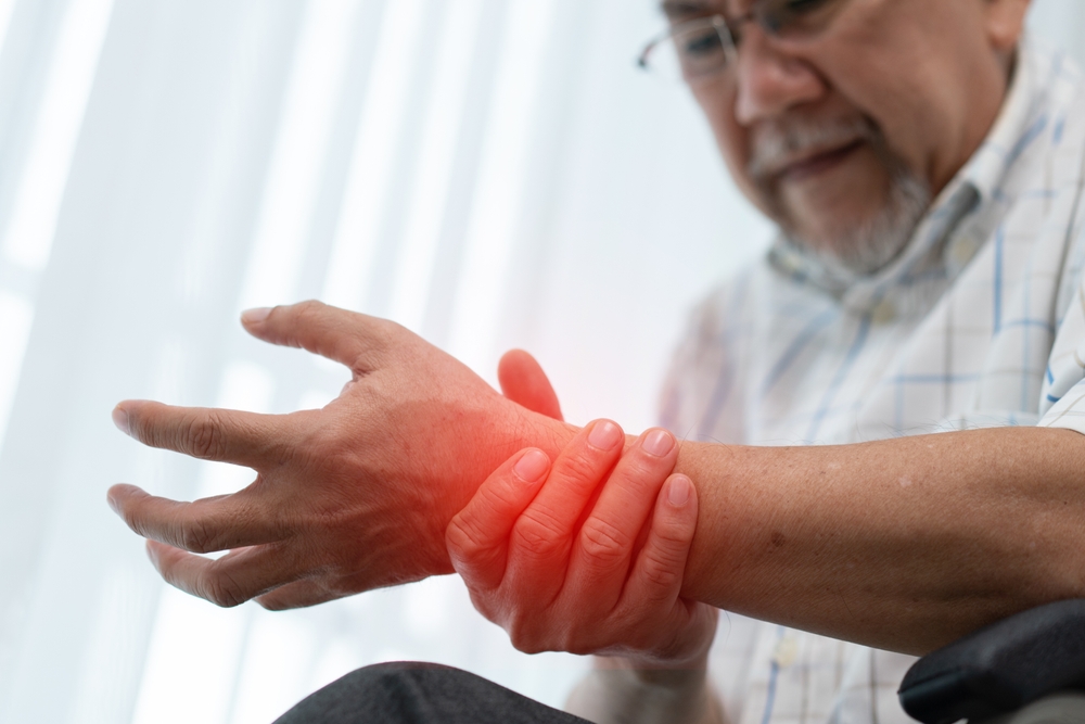A senior man holding his wrist with a red digital glow highlighting the joint to indicate inflammation or carpal tunnel pain.