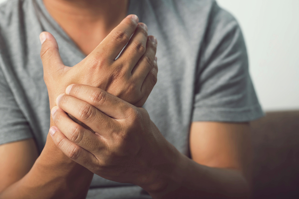 Close-up of a man holding and massaging his wrist with a look of physical discomfort to indicate wrist pain or numbness.