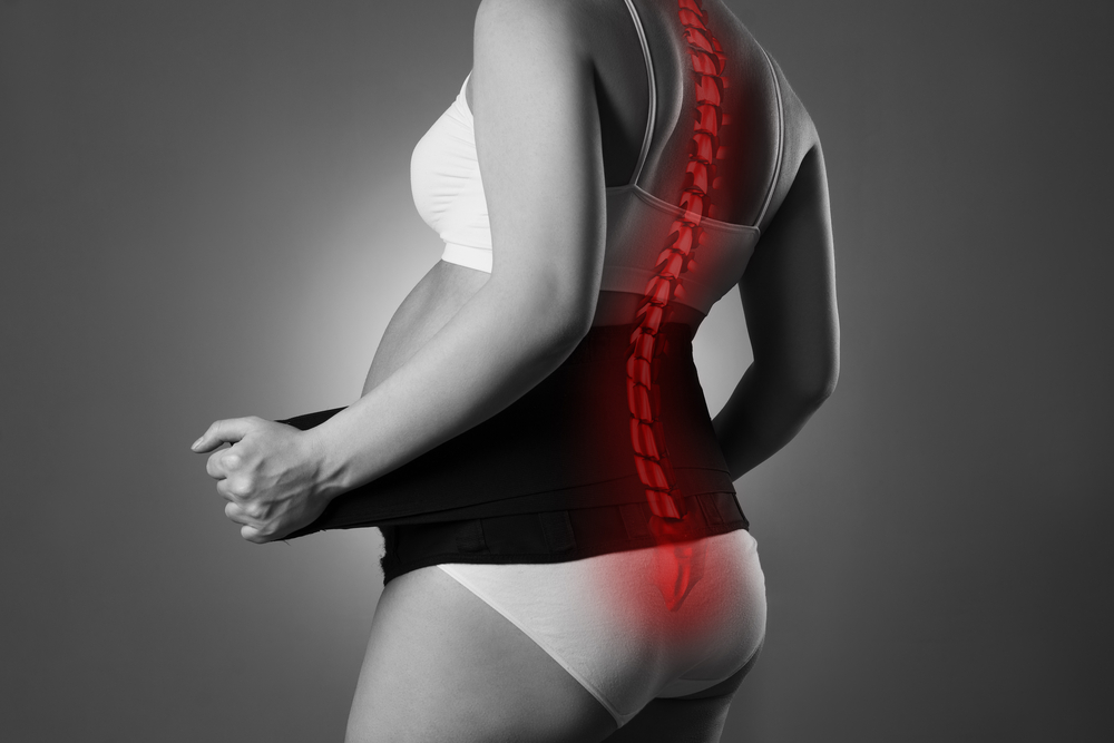 Black and white rear view of a pregnant woman wearing a maternity support belt with a red digital overlay showing a curved spine.