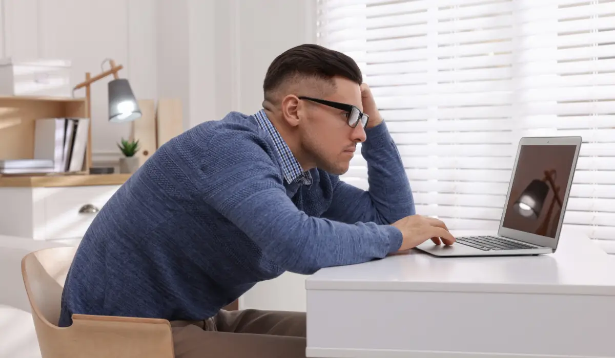 An office worker slouching at the laptop desk showing signs of boredom and tiredness, as sitting all day affects your spine and mood.