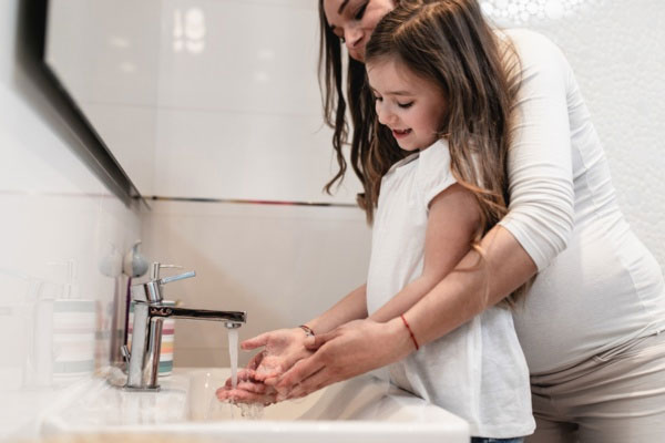 Woman and girl washing hands in bathroom sink.