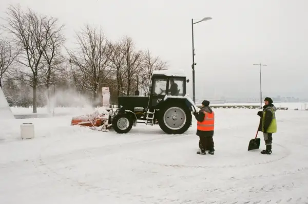 A tractor and two people in the snow.