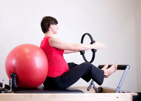 A woman sitting on a Pilates machine, using a ball for exercise