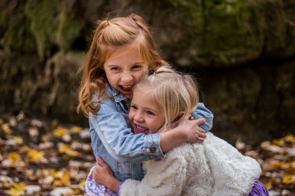 Two little girls embracing each other tightly amidst the colorful autumn foliage.
