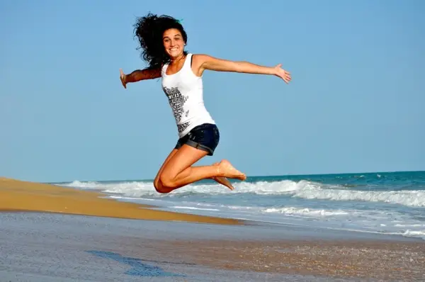Woman leaping joyfully on sandy beach.