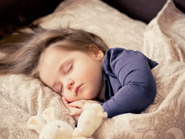 A little girl sleeping soundly in bed, cuddling a stuffed animal for comfort.