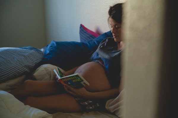 Pregnant woman reading book in bed.