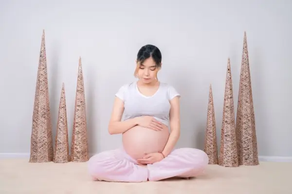Asian woman sitting on the floor, gently cradling her belly