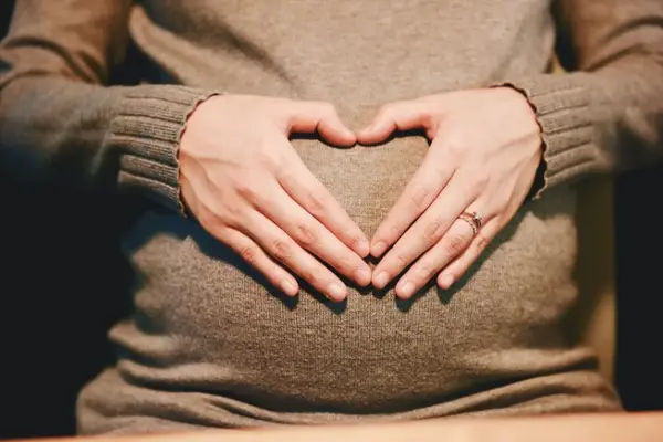 A pregnant woman cradling her belly in the shape of a heart