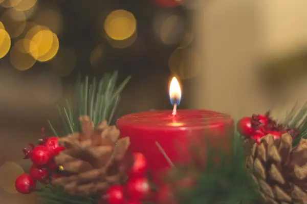 A festive red candle adorned with pine cones and berries.